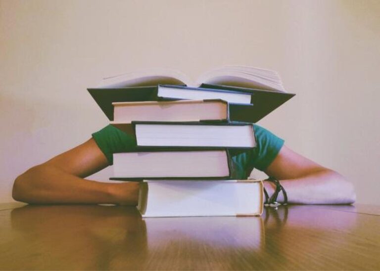 stack of books in front a person with arms crossed on a table