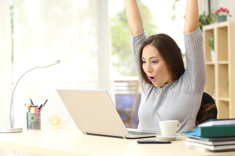 woman cheering at her desk looking at her laptop