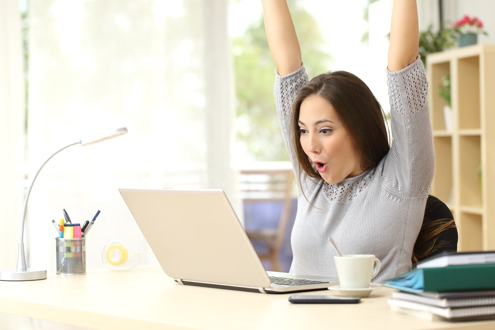 woman cheering at her desk looking at her laptop