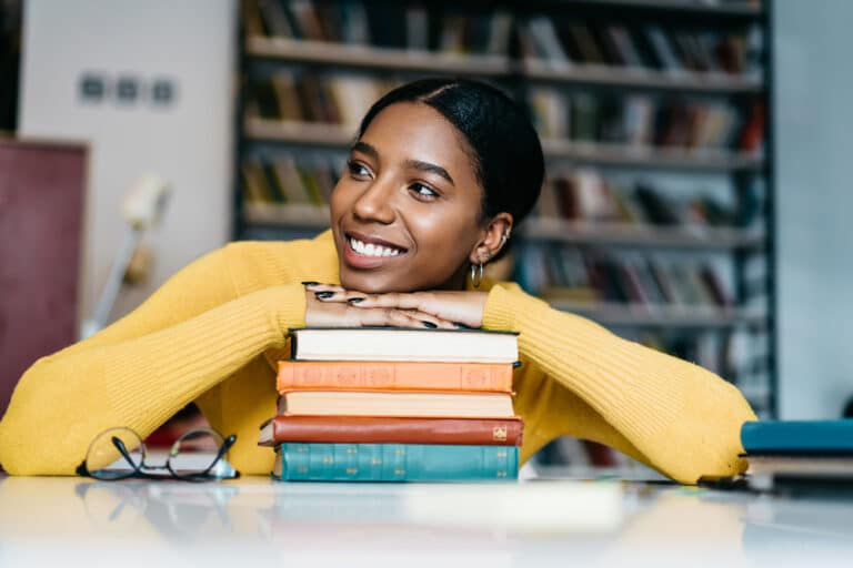 woman smiling and resting chin and hands on a stack of books