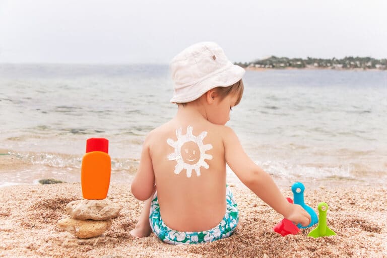 toddler sitting on the beach with toys