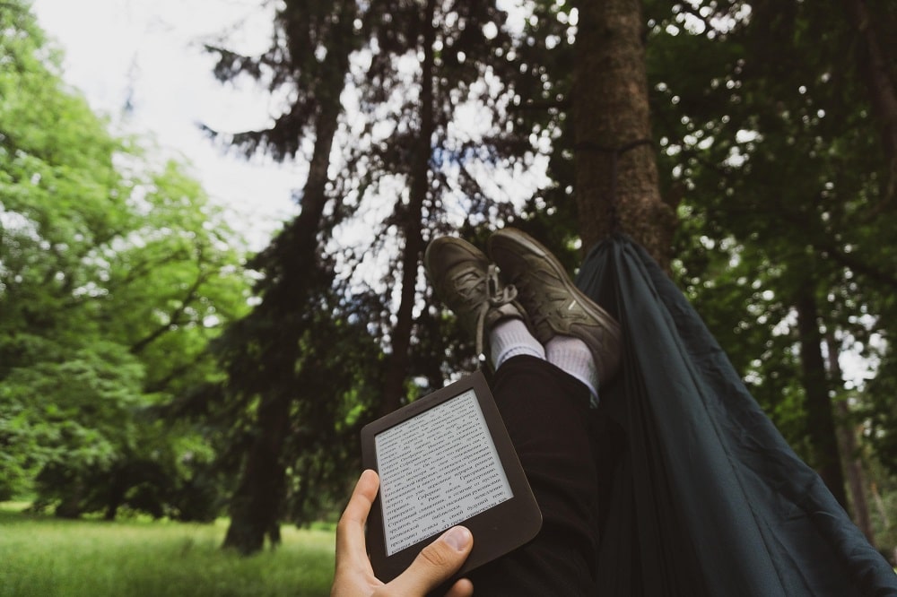 A person reading a Kindle lying in a hammock