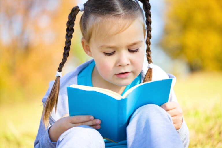 little girl reading blue book in field